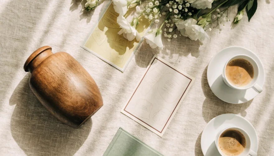 Flatlay met witte bloemen, houten urn, kaarten en koffiekopjes